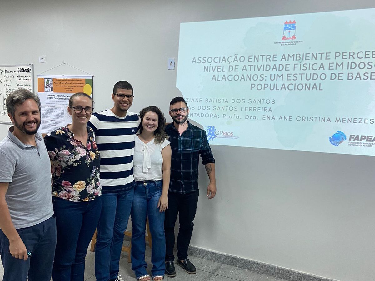Pessoas sorrindo com trabalho acadêmico no fundo intitulado "Associação entre ambiente percebido e nível de atividade física em idosos alagoanos: um estudo de base populacional."